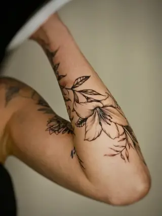 Duża lilia z pędami liści oplatająca przedramię i łokieć, czarne cieniowanie – tatuaż Oli, SHADY TATTOO Wieluń