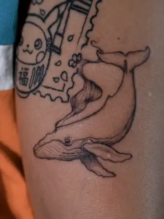 Wieloryb w czarnej kresce z cieniowaniem na ramieniu, powyżej fragment innego tatuażu w formie znaczka – tatuaż Oli, SHADY TATTOO Wieluń