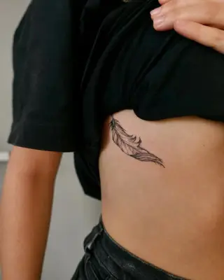Cienkie czarne pióro wytatuowane na żebrach z boku tułowia – tatuaż Zuzi, SHADY TATTOO Wieluń