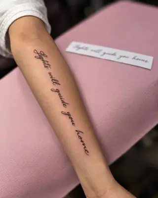 Tatuaż napis „lights will guide you home” odręczną kursywą wzdłuż przedramienia, obok wydruk szablonu