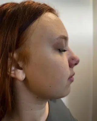 Świeży piercing nostril – mały kolczyk w nosie, profil klientki z rudymi włosami