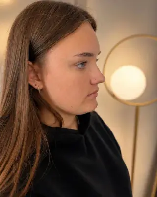 Delikatny piercing nostril, profil klientki z ciemnymi włosami na tle jasnego wnętrza