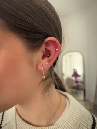 Piercing helix w górnej chrząstce ucha i kolczyki w płatku, klientka w beżowym swetrze