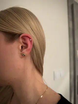 Ucho z przekłuciem helix i kolczykiem w płatku, blond włosy zaczesane za ucho, ujęcie z boku