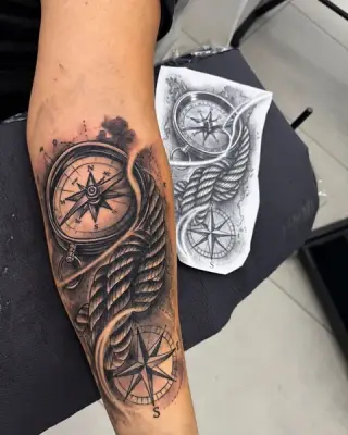 Tatuaż kompasu z róży wiatrów i liny na przedramieniu, black and grey, obok widoczny papierowy szkic projektu