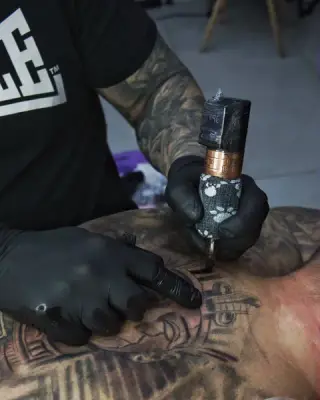 Tatuator SHADY TATTOO w Wieluniu podczas pracy maszynką nad dużym tatuażem plecowym, zbliżenie na dłonie w rękawiczkach